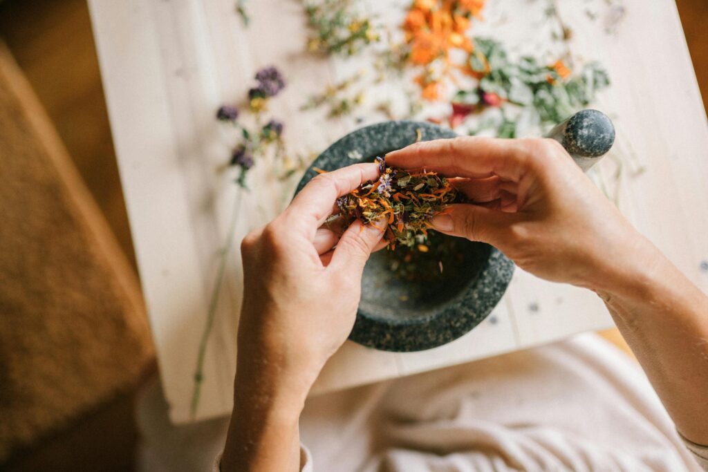 Close-up of hands mixing dried herbs with a mortar and pestle for herbal medicine preparation.